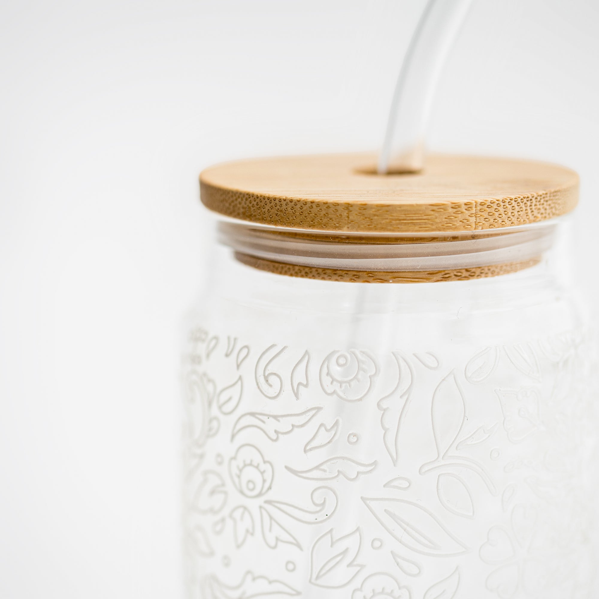 Close-up image of glass  straw tumbler with a floral design with the bamboo lid  on a white background. 