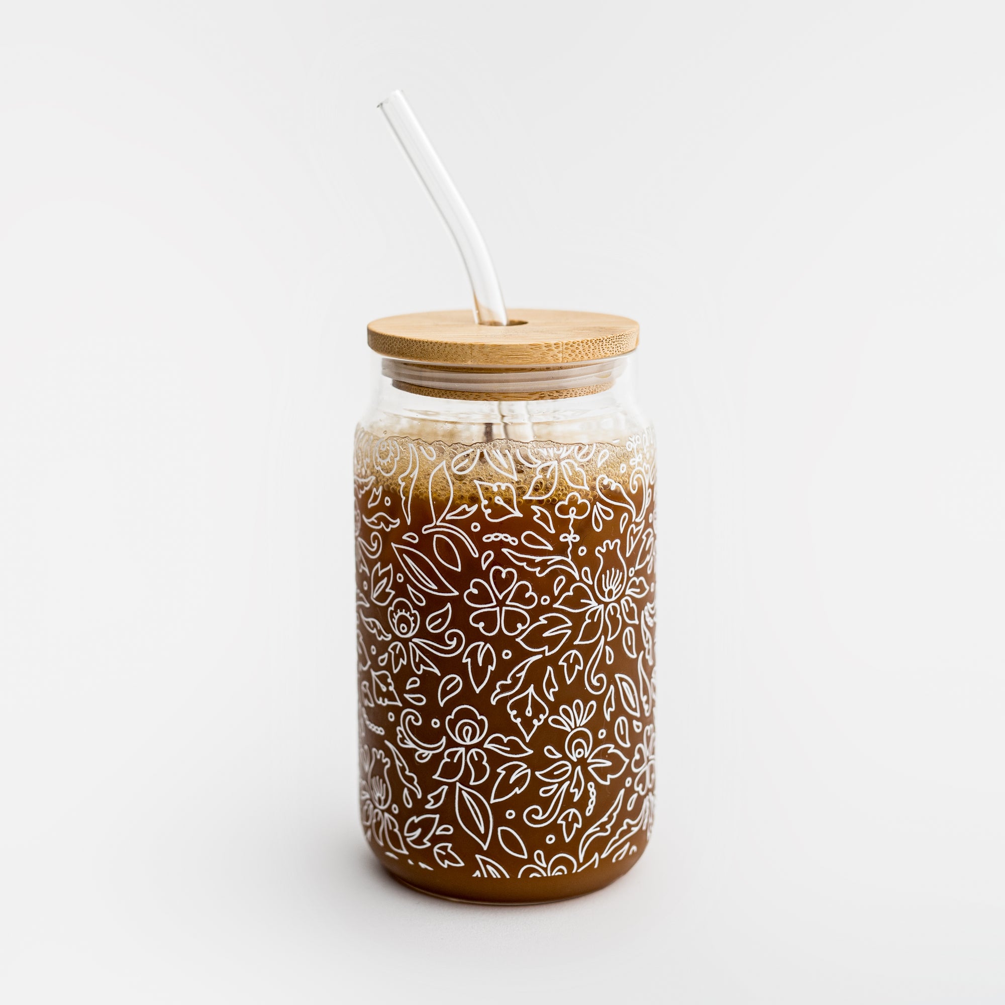 Image of glass  straw tumbler with a floral design with the bamboo lid  filled with iced coffee drink on a white background. 