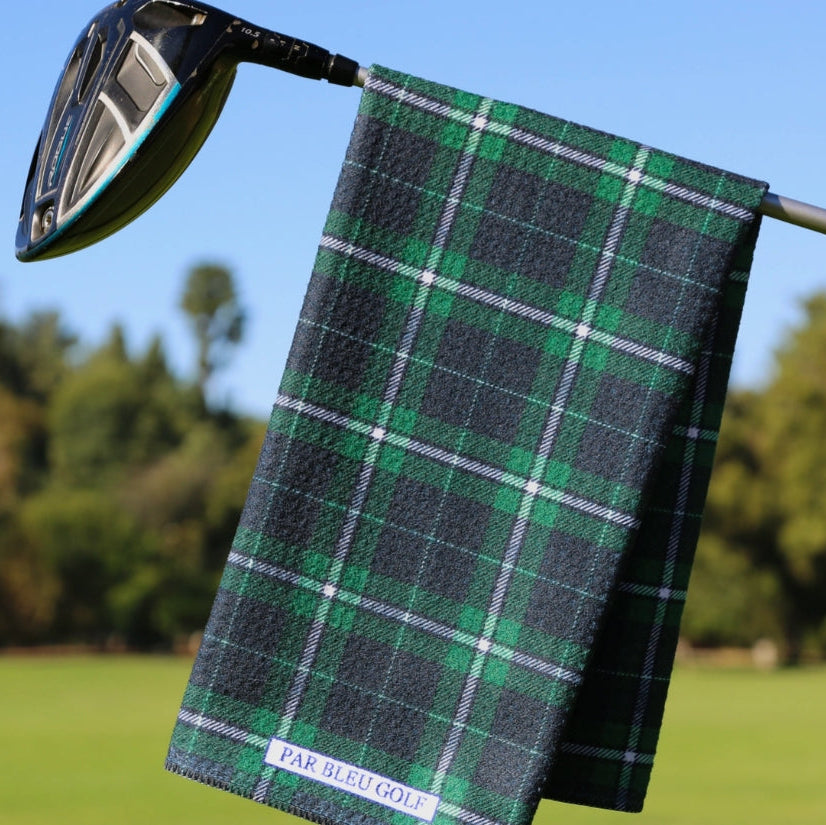 Green plaid golf towel hanging on a golf club with a blurred golf course background