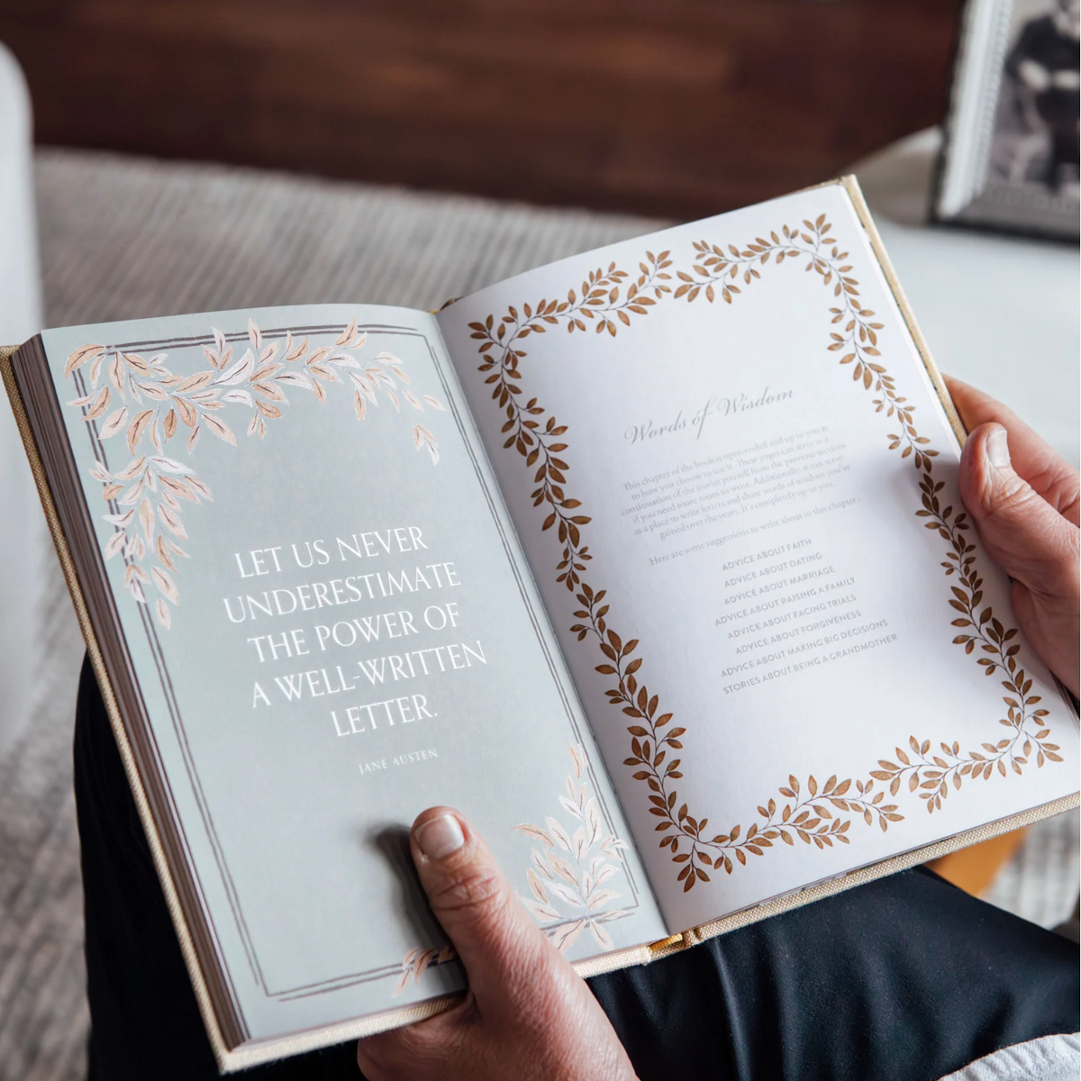 An open book held by two hands, showing printed pages with decorative leaf borders and a quote from Jane Austen on the left page.