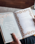 An open book held by two hands, showing printed pages with decorative leaf borders and a quote from Jane Austen on the left page.