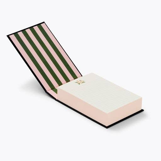 Hawthorne desktop notepad is featured propped open, with the cover slightly raised at an angle to display its striped interior pattern (pink and green) and the notepad's pages in display with a small floral decoration in the upper center, on a white background. 