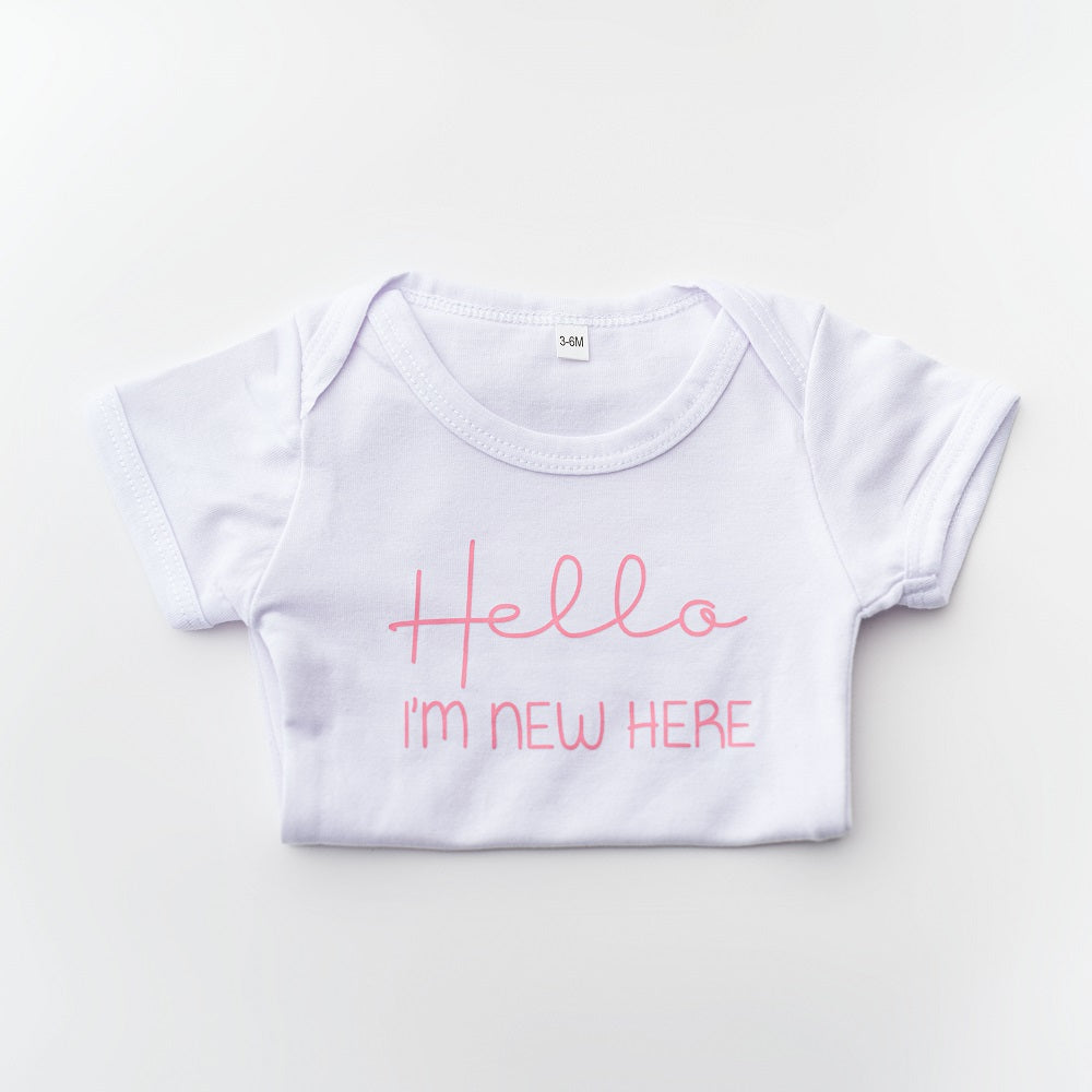 Hello, I'm new here. This onesie features pink vinyl lettering in a white onesie on a white background. 