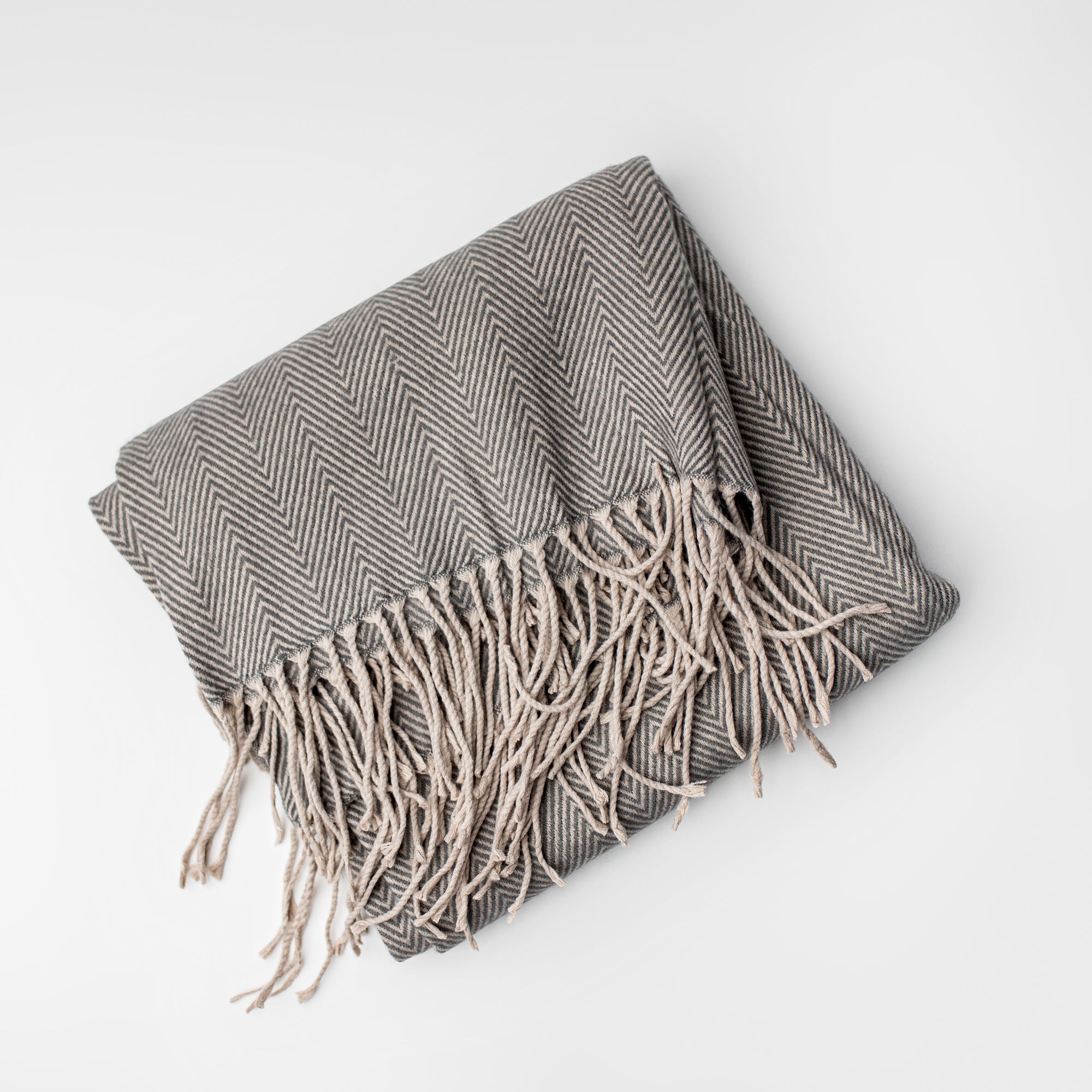 Herringbone throw blanket featured in its gray beige stripes and flakes form on a white background. 