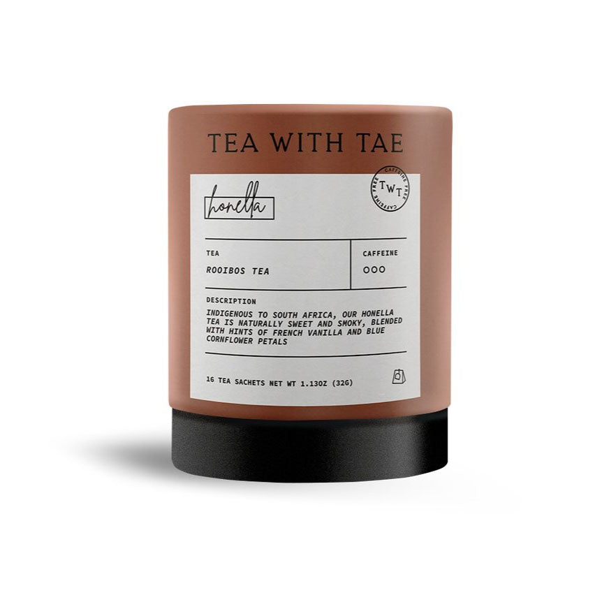A product image of a container of Rooibos tea, featuring the tea name "honella" and various details about the tea from the brand Tea with Tae.  a close-up, full shot of a cylindrical container, which is the primary focus. The container is a light reddish-brown color, and a dark black base. Presented on a plain, white background