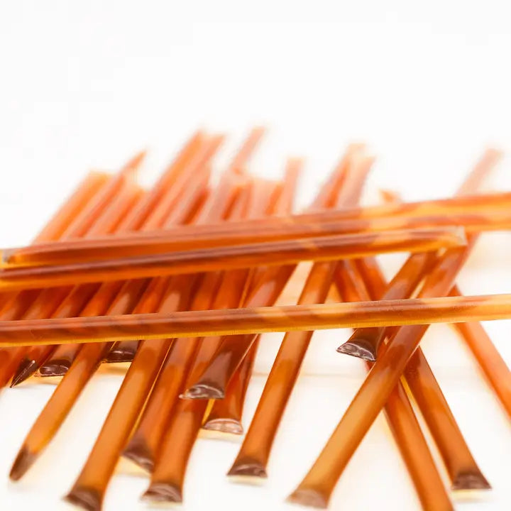Several honey straws are featured in their transparent rectangular plastic package showing the warm brown honey inside on a white background. 