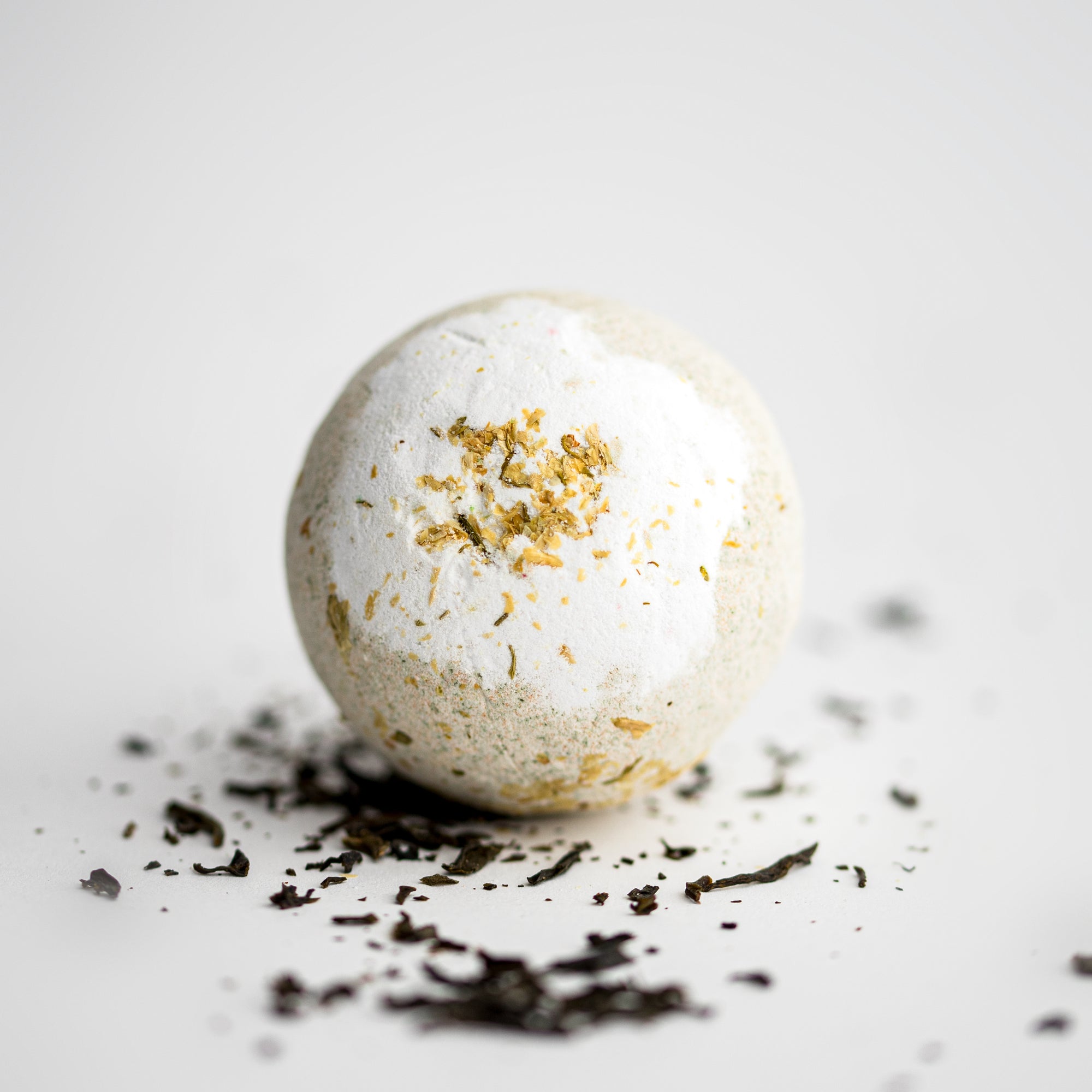 Jasmine bath bomb featured in its round shape and details, surrounded by jasmine pieces on a white background. 