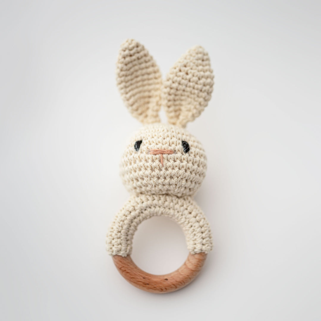 Crocheted bunny rattle with wooden ring on a light gray background