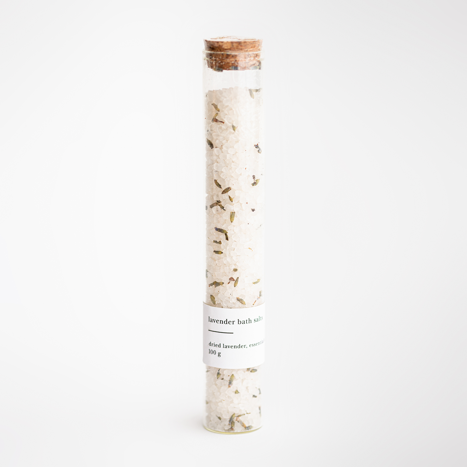 Lavender bath salts featured in their transparent container with a cork lid and white label with black lettering. 