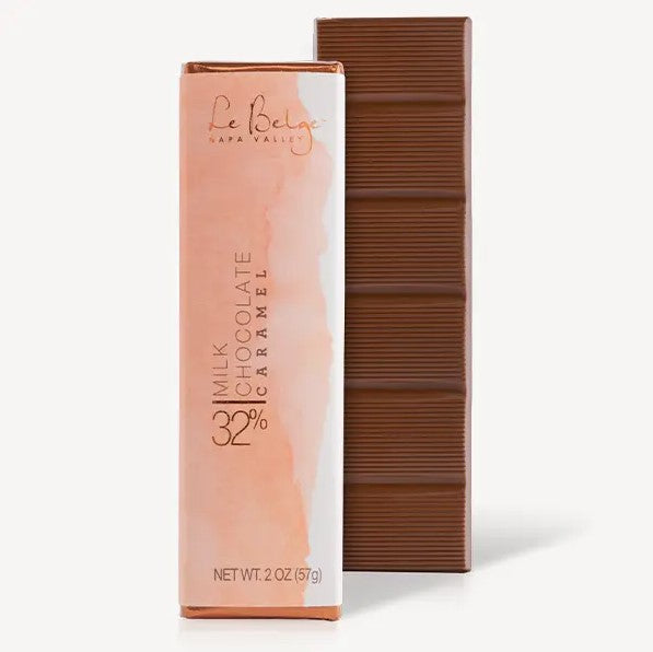 The image showcases two rectangular bars of chocolate, one wrapped  and one unwrapped. The unwrapped chocolate bar displays a rich, brown hue with visible rectangular indentations, typical of chocolate bars. The wrapped bar is in a package with a soft peach-colored gradient, likely representing the flavor profile. The package features text indicating "Milk Chocolate Caramel 32%" and "Le Belge Napa Valley." The bars are clean, well-defined, and present a premium appearance.