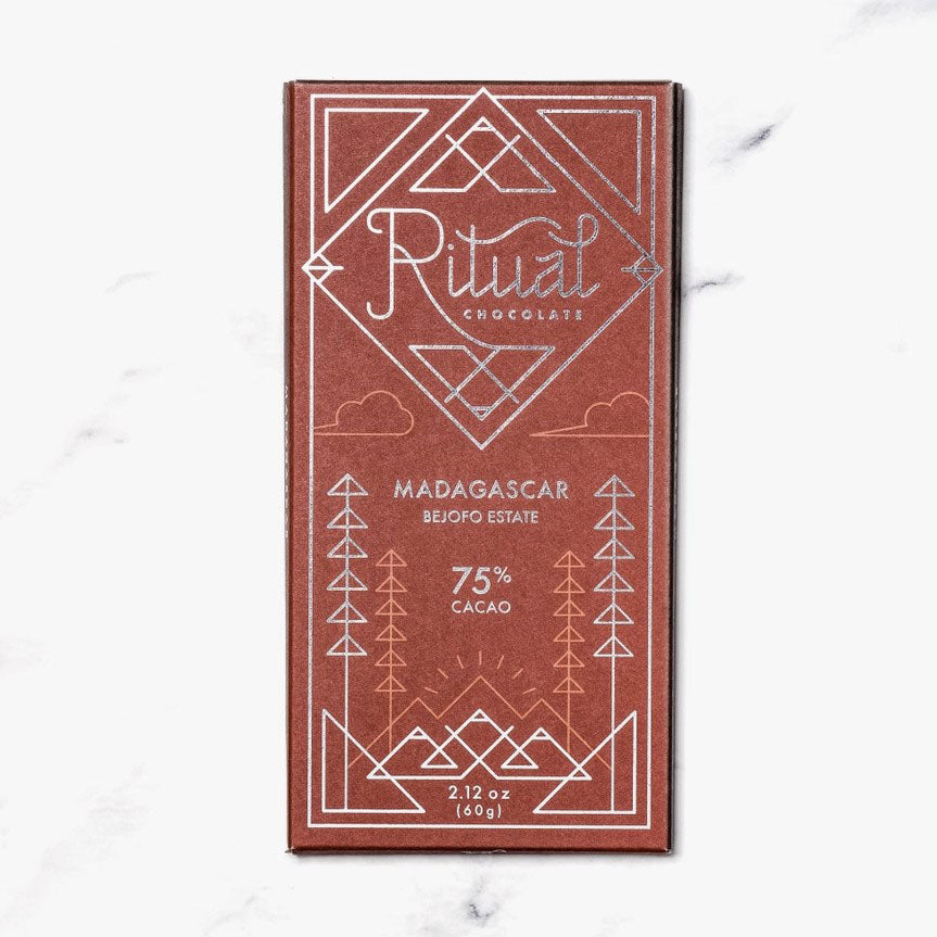 Ritual Madagascar Bejofo estate chocolate bar featured in tis terracot wrapping with geometrical patterns and text elements in two different colors silver and orange.The background, a marble-like surface.