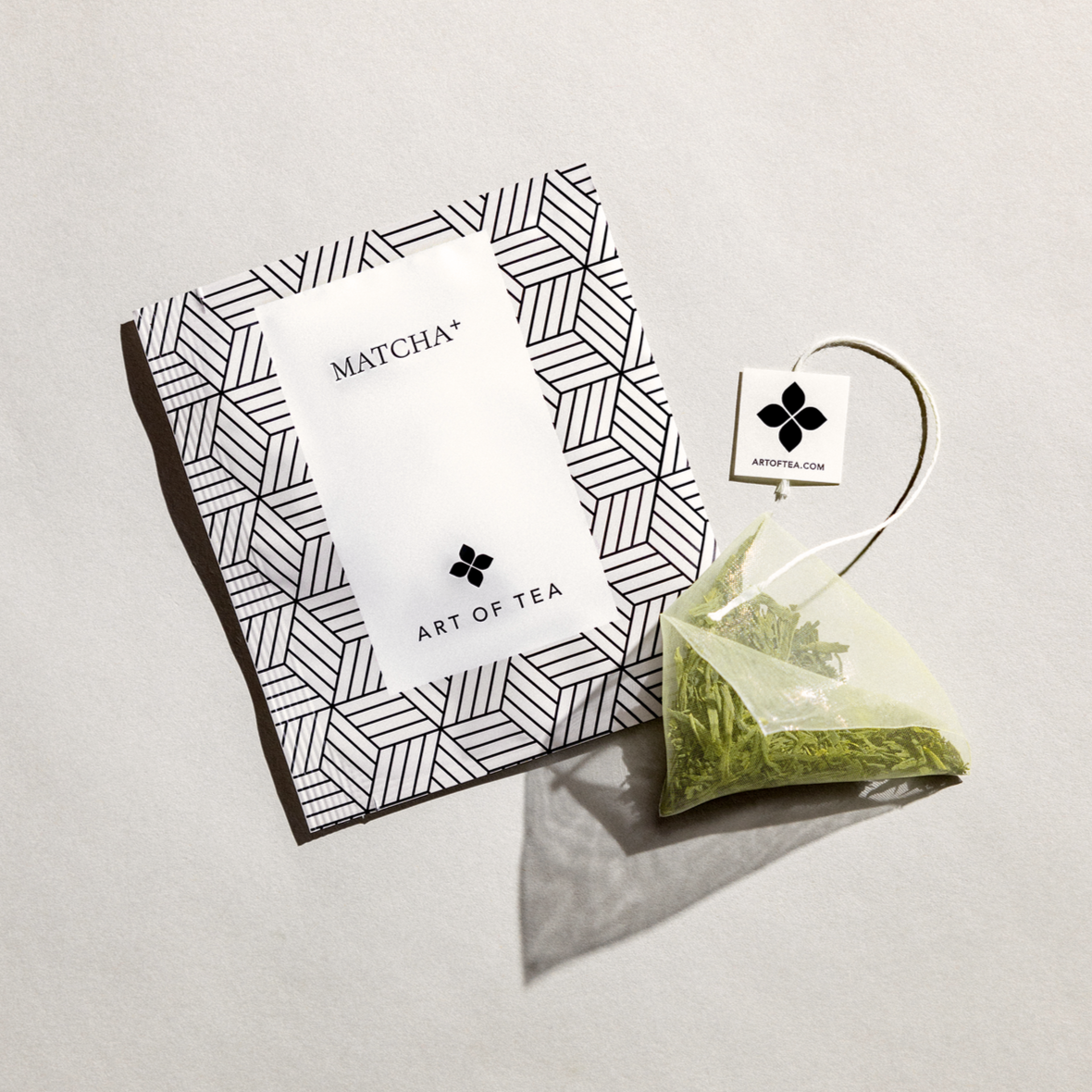 Matcha Tea Sachet from art of tea, featured in its sachet black geometric lines, white label and black lettering. next to the sachet outside in its transparent bag and green leaves.