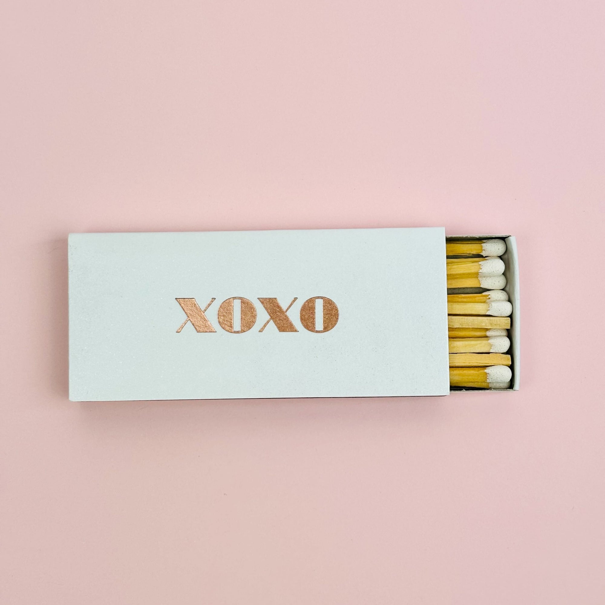 White matchbox with metalic rose gold lettering XOXO, includes matches with white tip. 