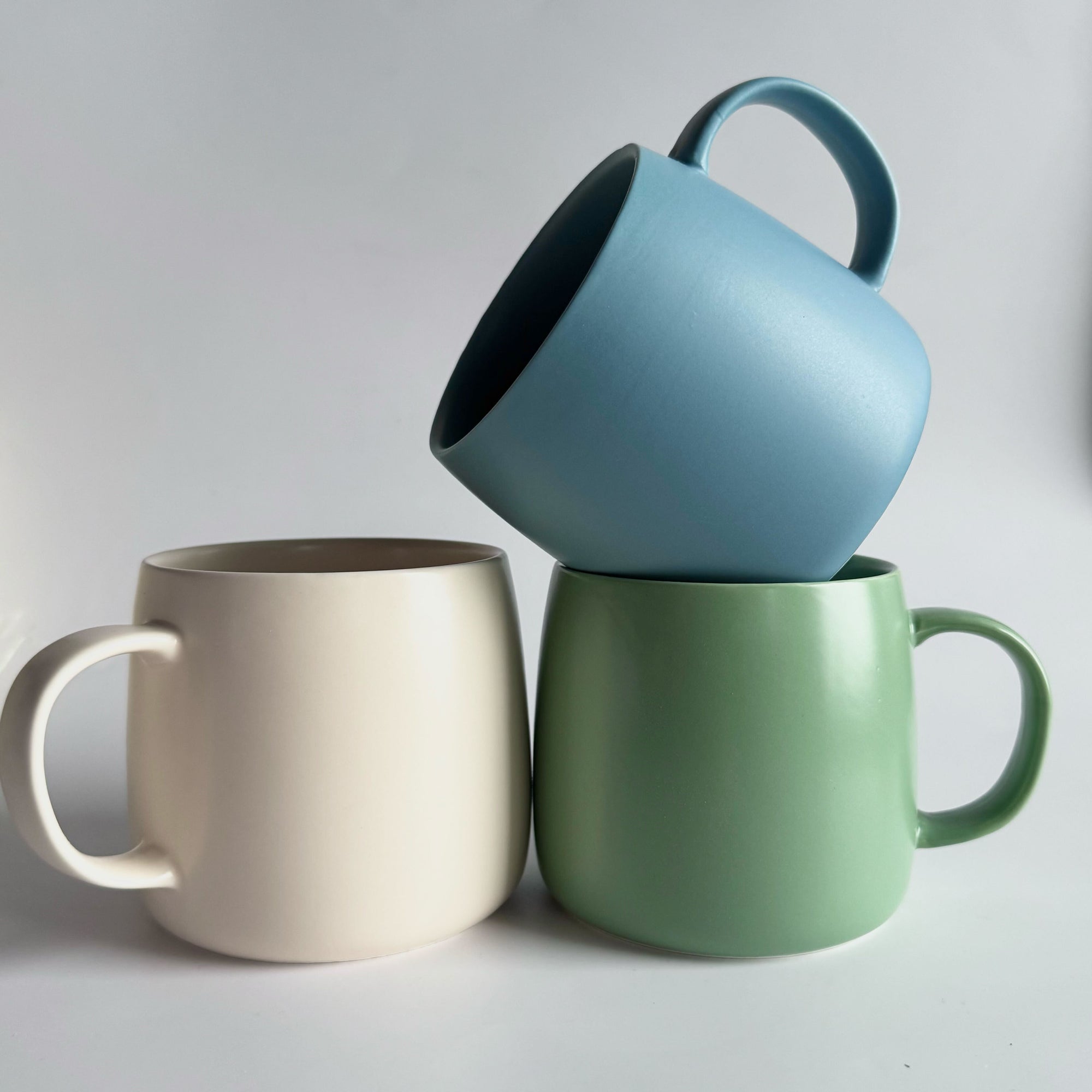 Three mugs in blue, beige, and green on a light gray background