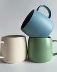 Three mugs in blue, beige, and green on a light gray background