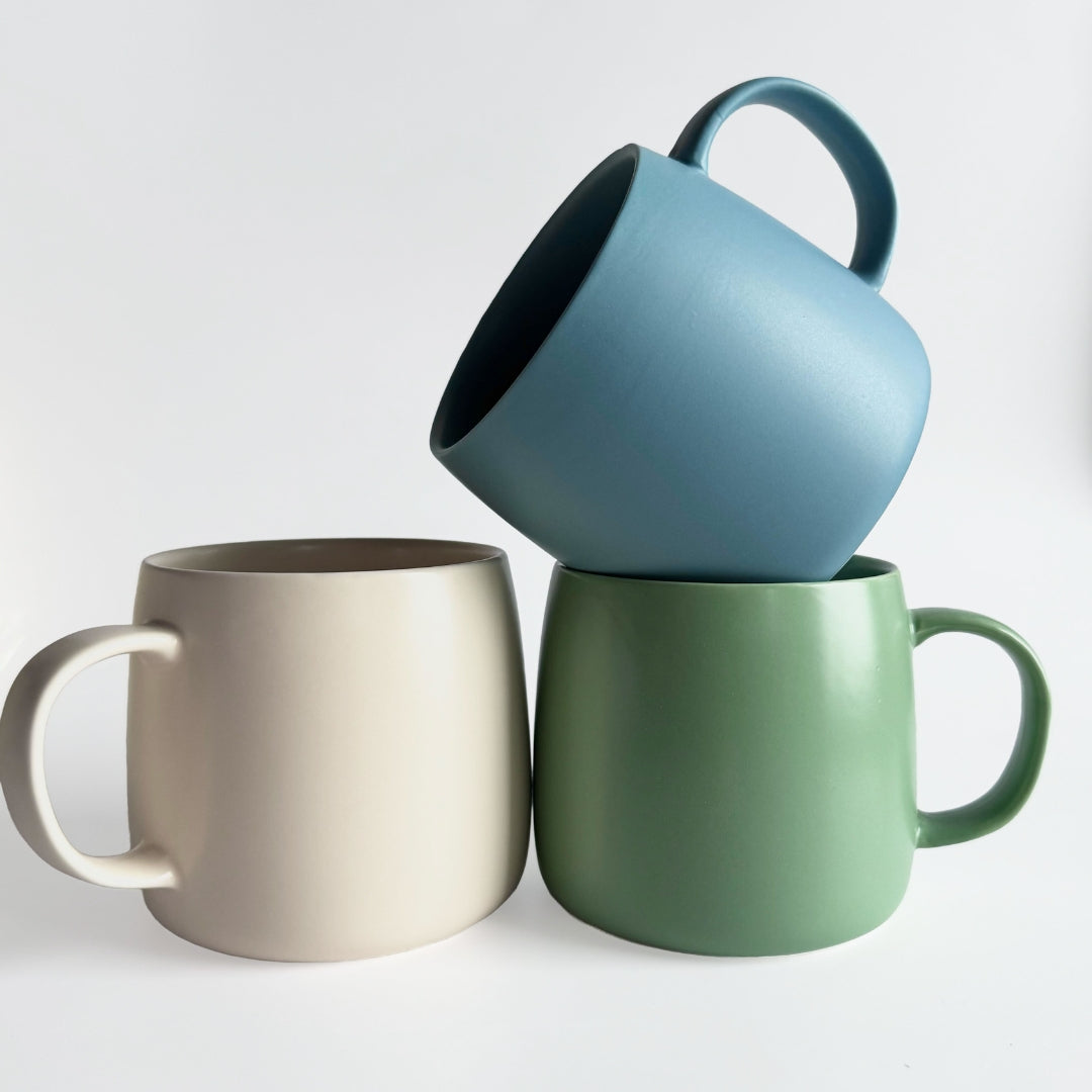 Three mugs in blue, green, and beige on a white background