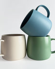 Three mugs in blue, green, and beige on a white background
