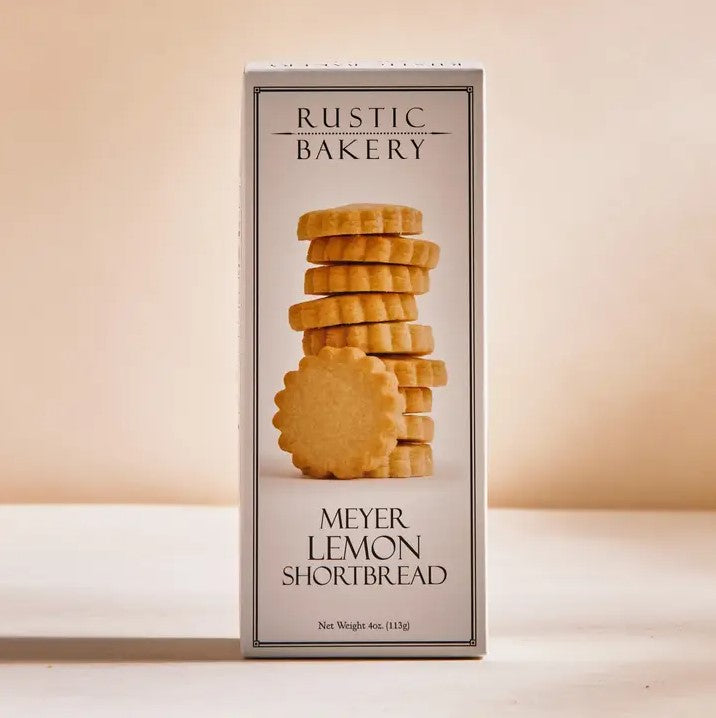 Meyer lemon shortbread cookies are featured in their white box rectangular-shaped box that has the image of the cookies and the information and title in black lettering with black lines border with white background in beige shadow lighting. 