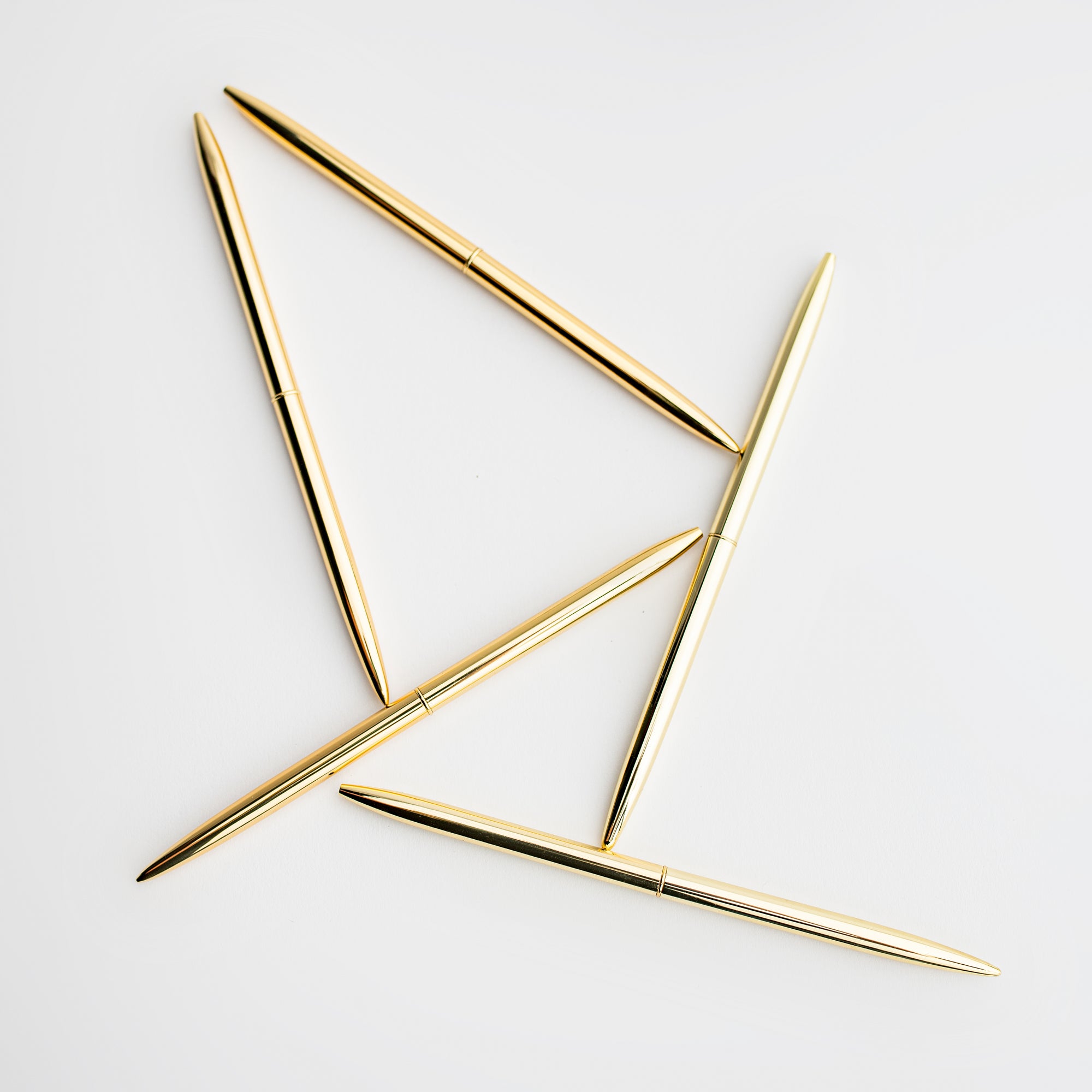 Five minimalist gold pens are featured on a white background.