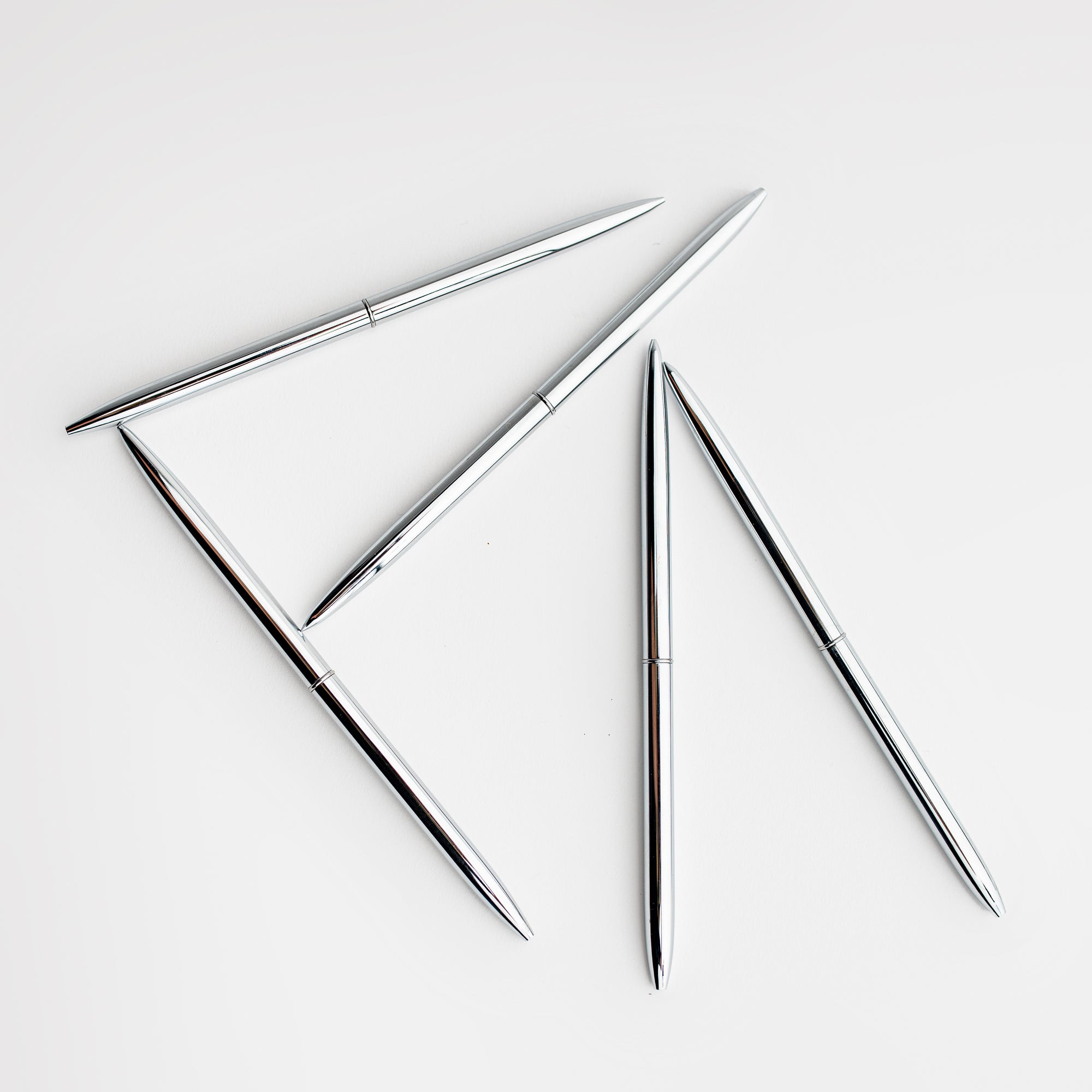 Five minimalist silver pens that have a round shape are featured on a white background.