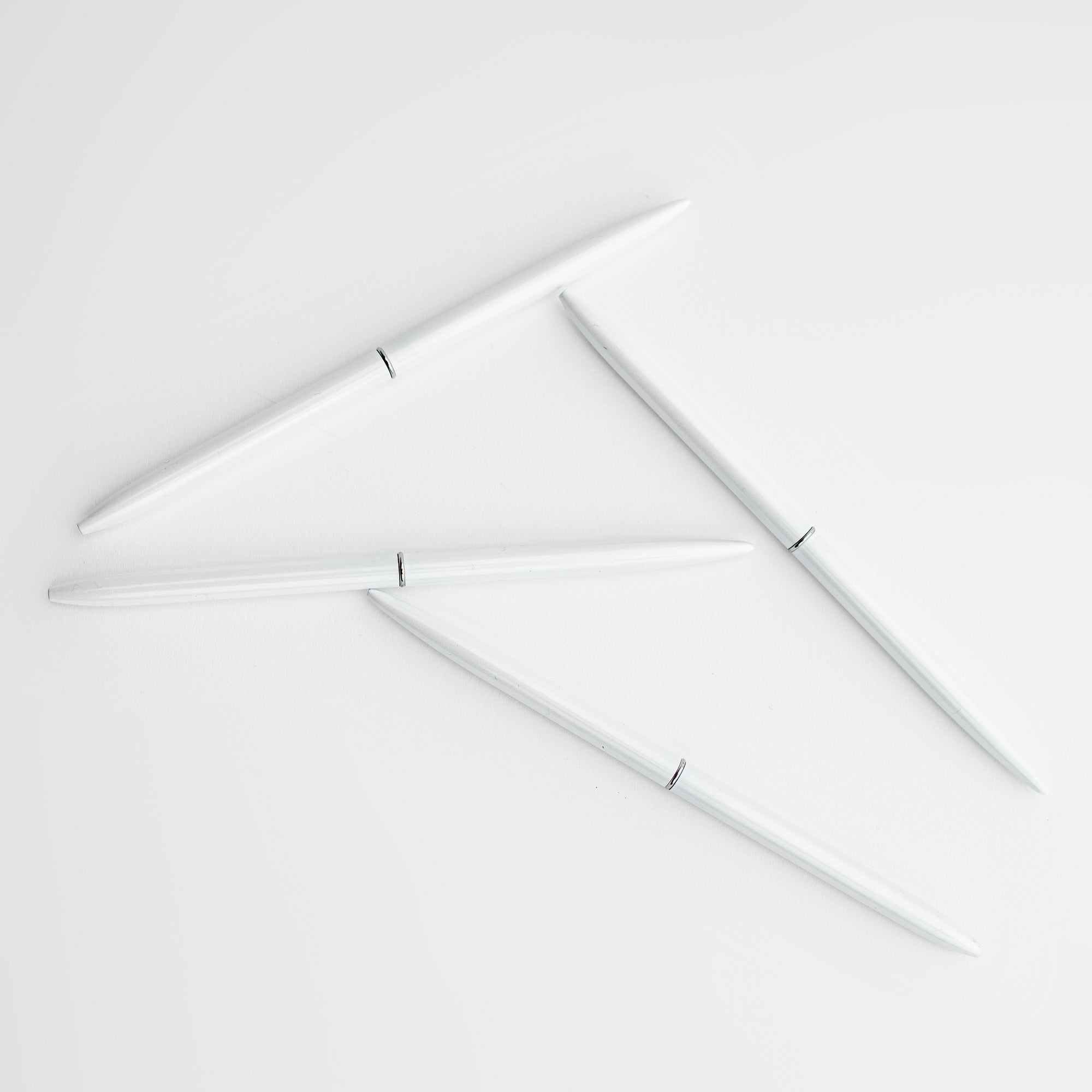 Minimalist white pen featured 4 of them in their circular form and silver band detail on a white background. 