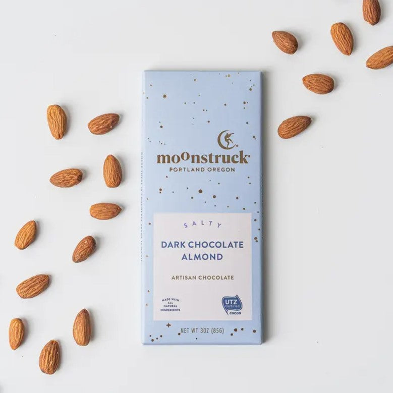 Moonstruck dark chocolate almond featured in its rectangular light blue package gold lettering, white label with blue lettering on a white background with almonds around.