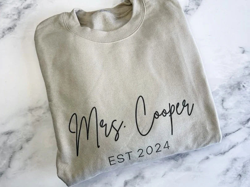 Mrs. established custom sweatshirt in sand color in black lettering personalized with Mrs. Cooper Est. 2024 in a marble like background. 