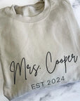 Mrs. established custom sweatshirt in sand color in black lettering personalized with Mrs. Cooper Est. 2024 in a marble like background. 