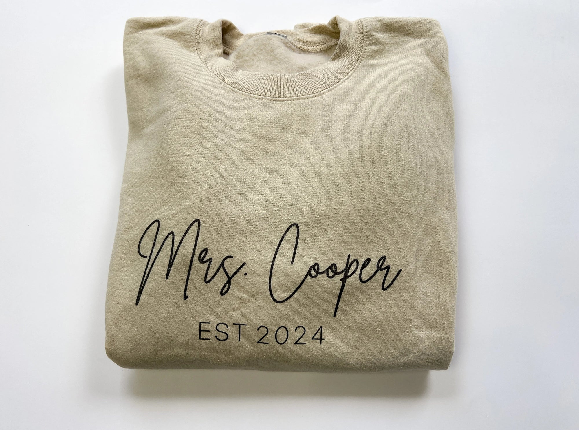 Mrs. established custom sweatshirt in sand color in black lettering personalized with Mrs. Cooper Est. 2024 in a white background.
