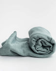 Muslin swaddle blanket in sage color featured on a white background. 