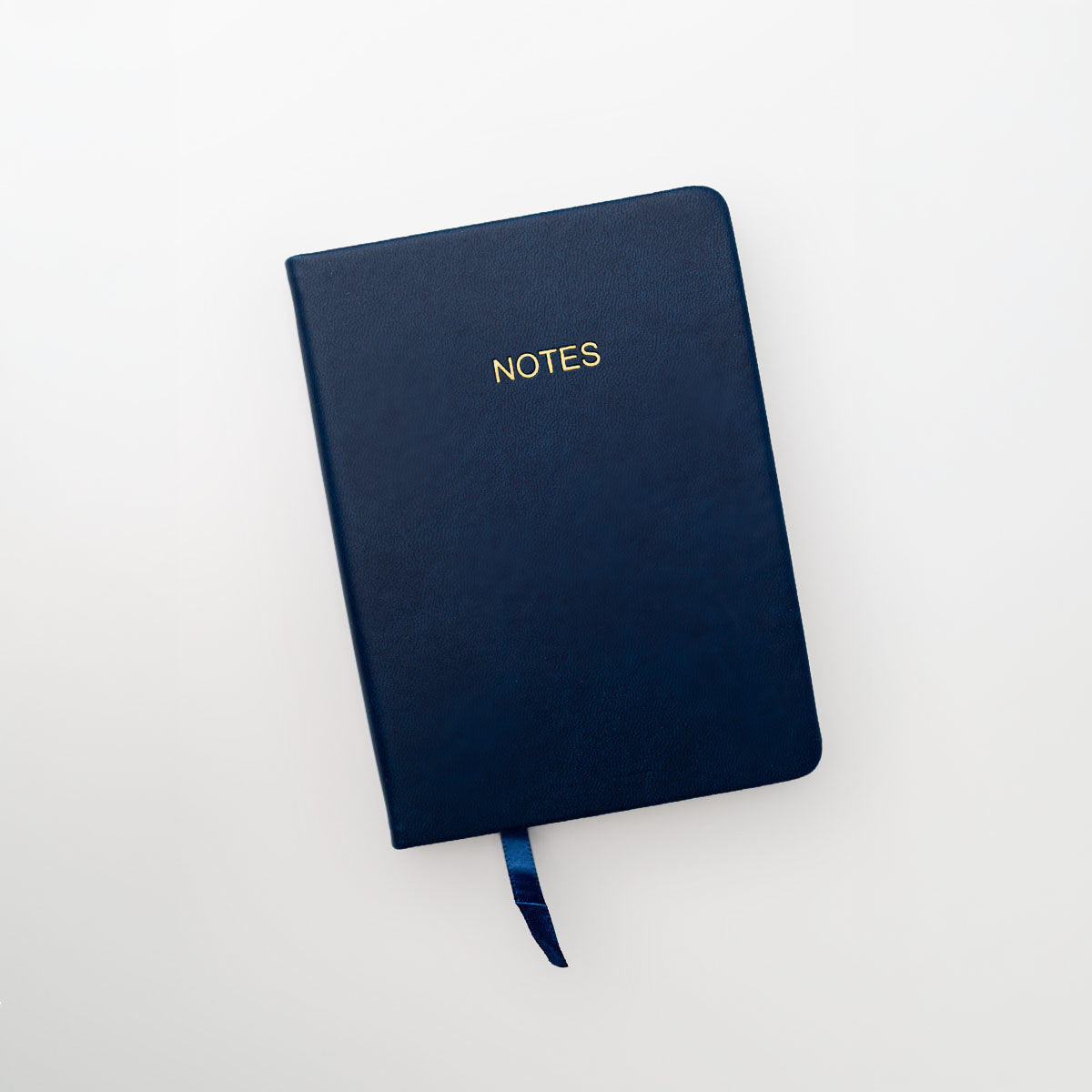 A navy blue hardcover notebook with gold foil lettering that reads 'NOTES' on the front cover, shown on a clean white background with a matching navy ribbon bookmark.