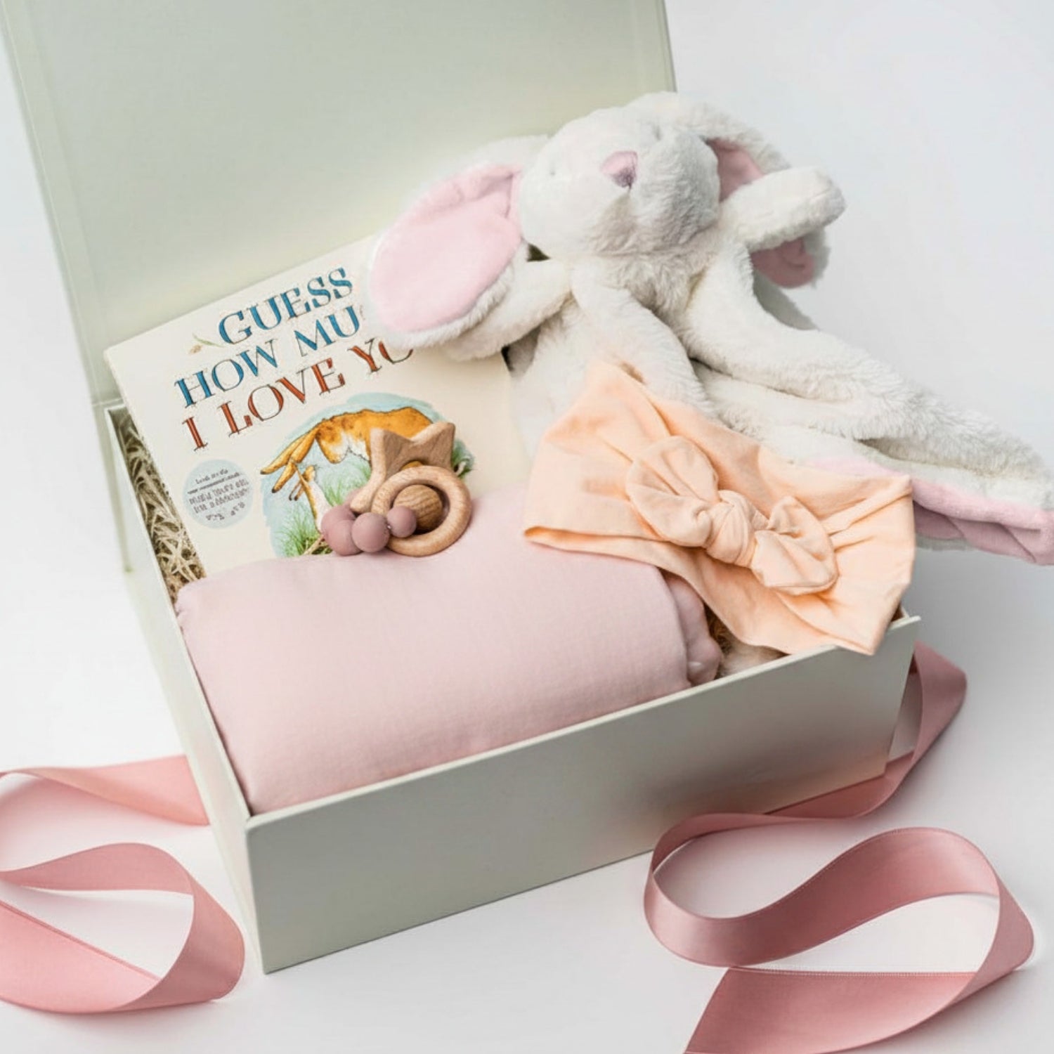Gift box with baby items including a plush toy, blanket, and book on a white background