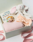 Gift box with baby items including a plush toy, blanket, and book on a white background
