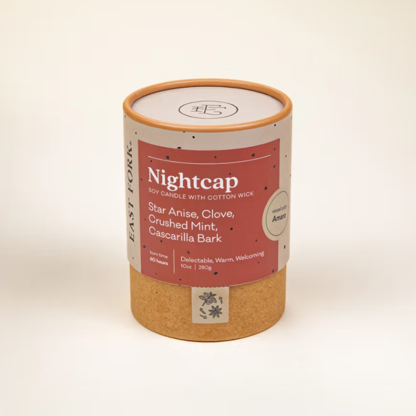 Nightcap candle is featured in its cylindrical container with tan bottom pink label and white lettering on a white background. 