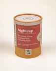 Nightcap candle is featured in its cylindrical container with tan bottom pink label and white lettering on a white background. 