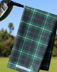 Green plaid golf towel hanging on a golf club with a blurred golf course background