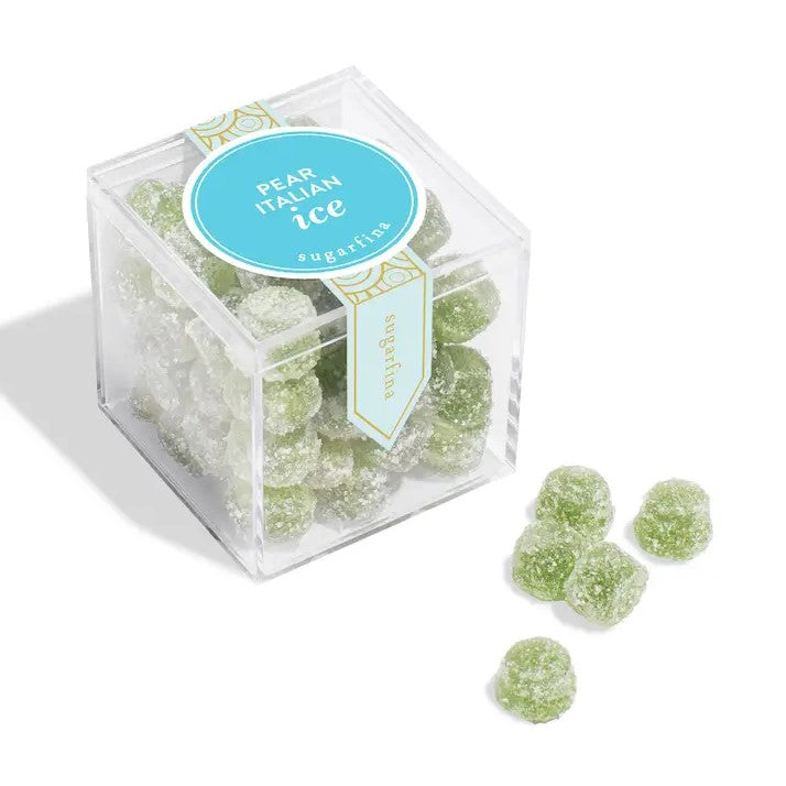 Sugarfina pear Italian ice cube is featured in its transparent square shaped container with its blue and gold details label and white lettering, revealing the green round gummies inside and in front of it 5 loose gummies all of this on a white background. 