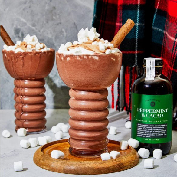 Image of the peppermint and cacao bottle with a drink of hot chocolate next to it and marshmallows. 