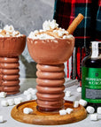 Image of the peppermint and cacao bottle with a drink of hot chocolate next to it and marshmallows. 
