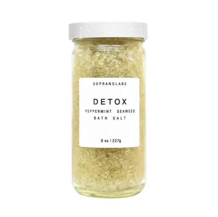 Peppermint detox bath salts is featured in its transparent with white lid jar showcasing the yellow salts with a white label with black lettering on a white background. 