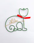 Personalized cat ornament, featuring an image of a cat crafted from green wire that forms the outline of a cat's body and head, complete with a red bow and a silver bell. In the center is personalized with the name Loki in gold aluminum wire. 
