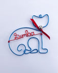 Personalized cat ornament, featuring an image of a cat crafted from turquoise wire that forms the outline of a cat's body and head, complete with a red bow and a silver bell. In the center is personalized with the name Sumba in red aluminum wire. 