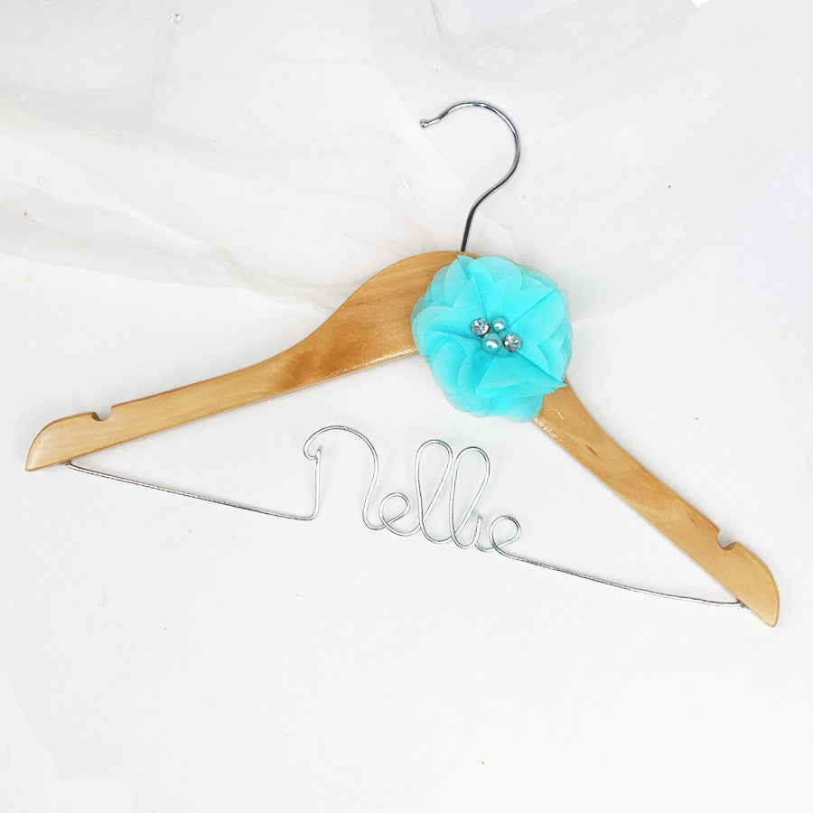 Light wood hanger with silver hook personalized in silver aluminum Nellie with a aqua chiffon flower on a white background. 
