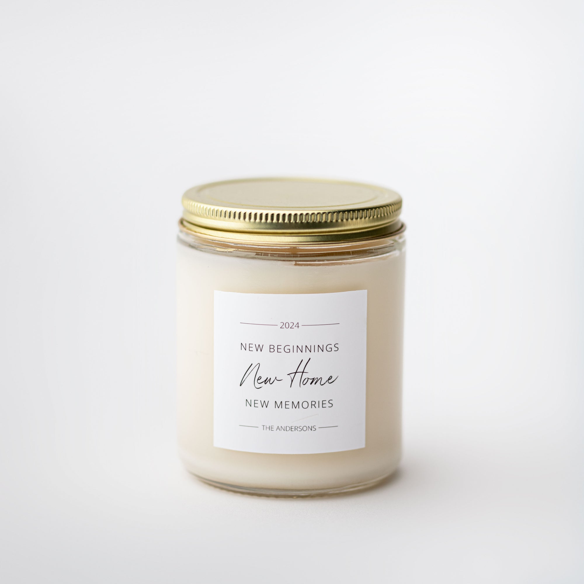Personalized housewarming candle is featured in transparent jar with gold lid and white label with black lettering, this one is personalized with the year 2024, New Beginnings, New Home, New Memories, and The Andersons.
