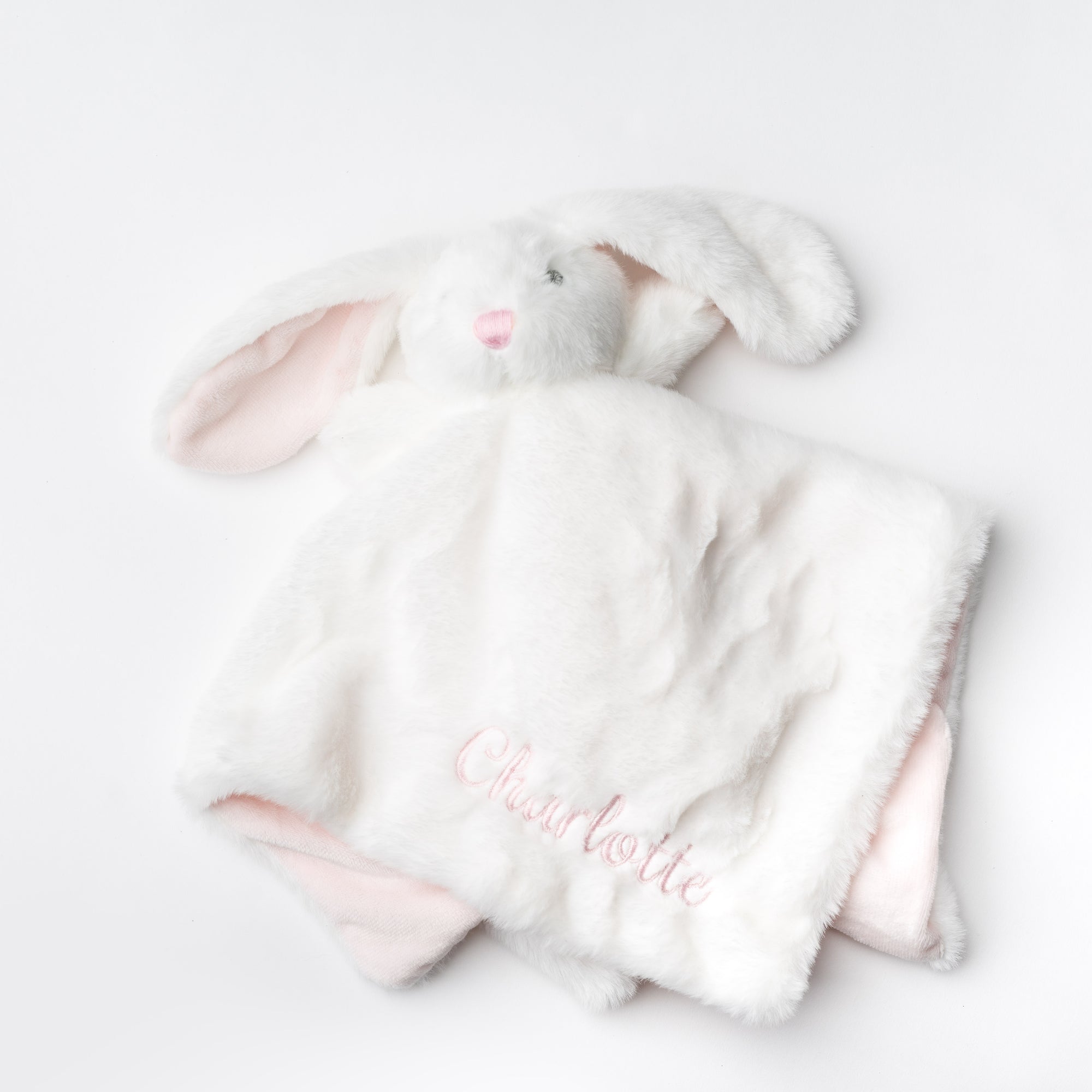 A soft, white, plush bunny security blanket with pink accents and the name "Charlotte" embroidered on it is presented against a bright white backdrop.