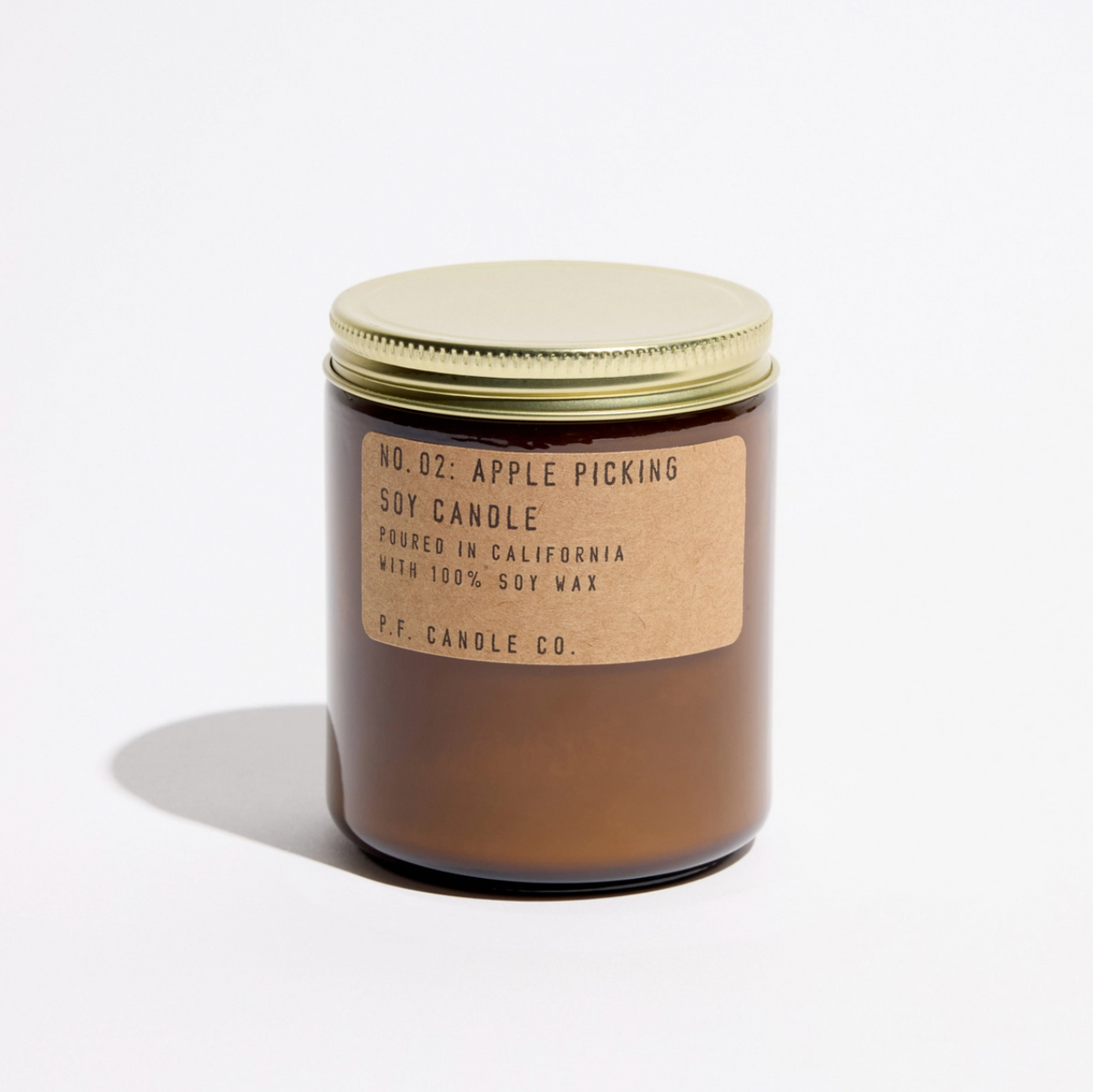 A single amber glass jar candle with a gold metal lid and a kraft paper label reading 'NO. 02: APPLE PICKING' and 'P.