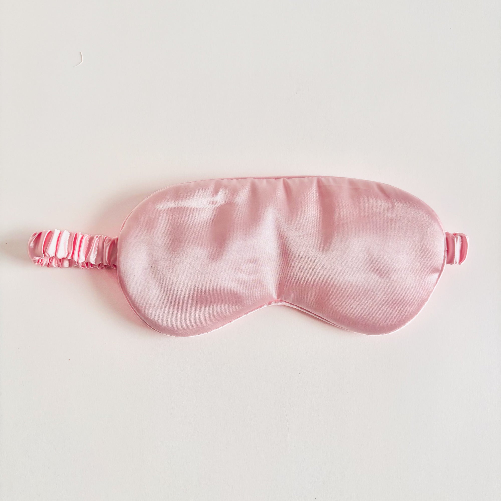 Pink satin sleep mask is featured on a white background. 