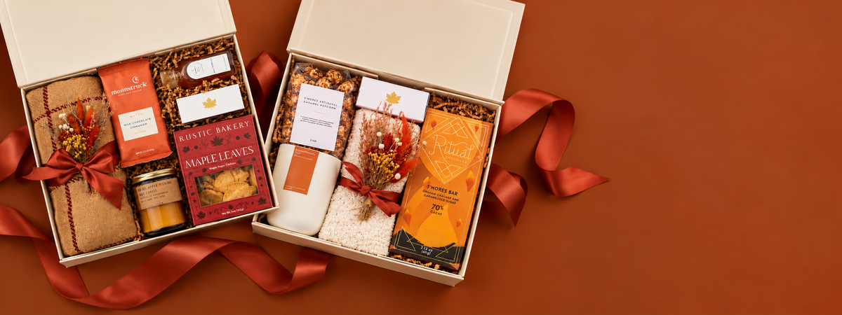 Two open gift boxes filled with assorted packaged treats and spa items, arranged on a warm brown background with red ribbon accents. The contents include wrapped items, a jar, and an orange packet.