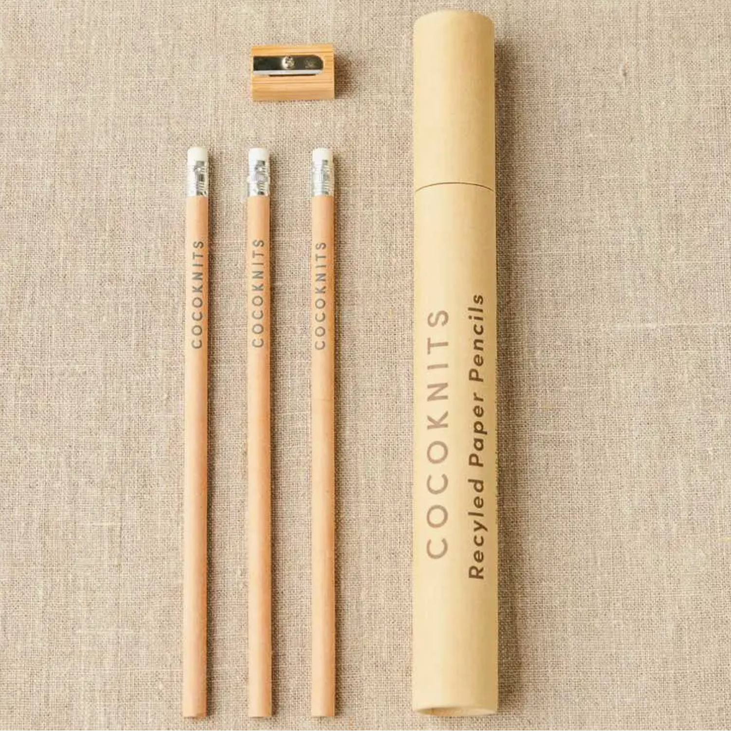 Set of recycled paper pencils with a sharpener and packaging on a textured beige background