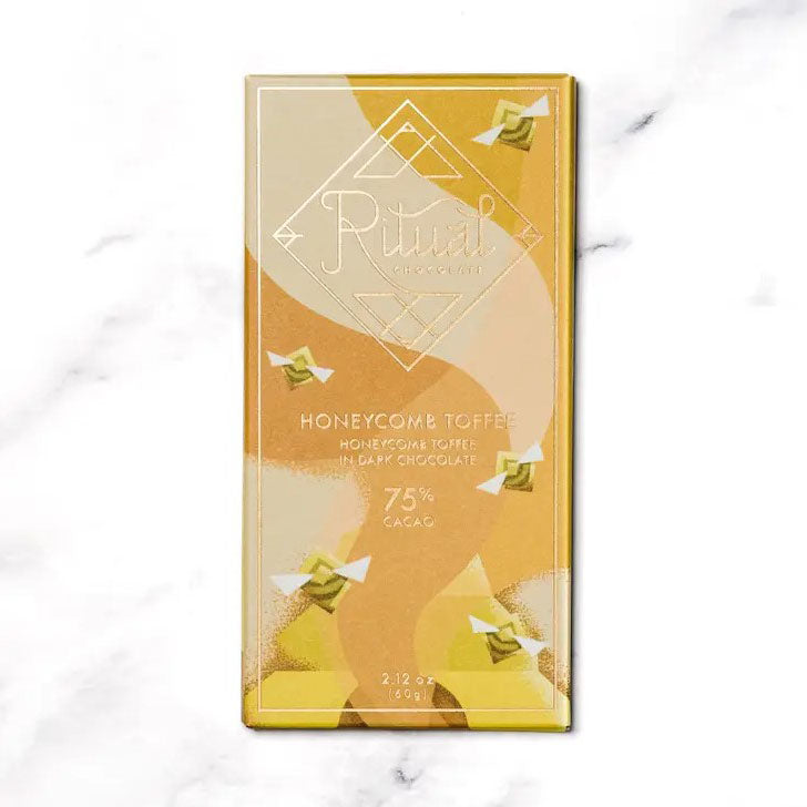 Honeycomb Ritual chocolate bar,A gold and beige packaging for a honeycomb toffee dark chocolate bar from Ritual. The image displays a predominantly gold and beige color scheme with a graphic design that features stylized honeycomb shapes.